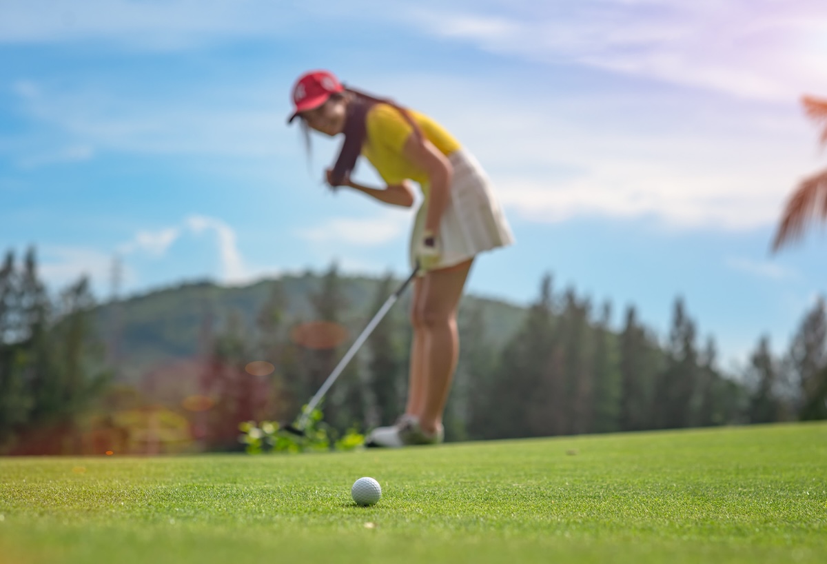 woman golfer in action of exciting of flowing of golf ball run almost to golf hole on the green