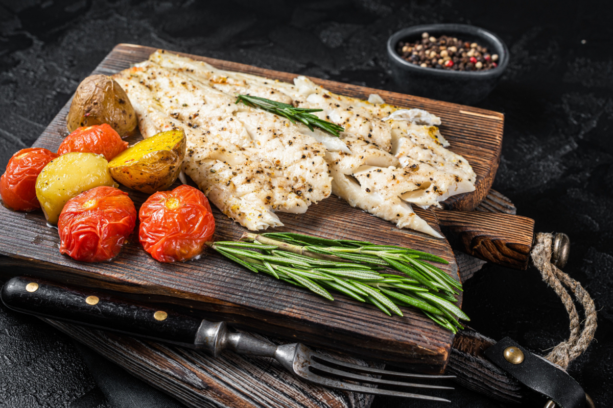 - DiningOut Baked Haddock fish fillet on wooden board with tomato and potato