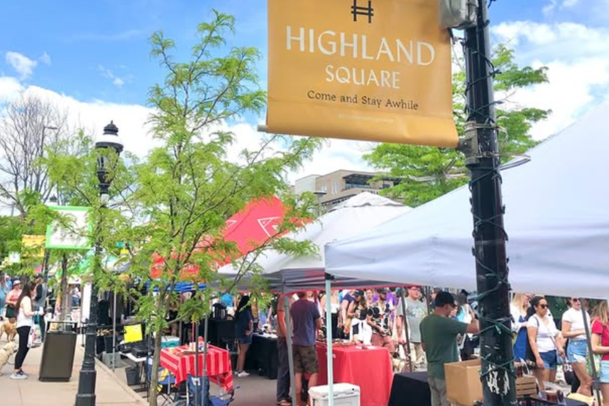 Highlands Square Farmers Market in Denver with vendor tents lining the sidewalk, shoppers browsing under a clear blue sky, and trees adding shade to the scene.
