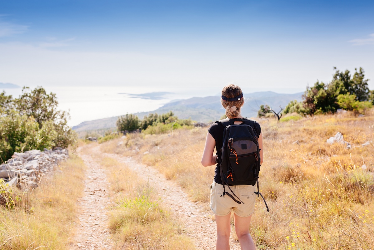 Young woman with backpack at mountain trail. Sveti Nikola mount, Hvar Island, Croatia