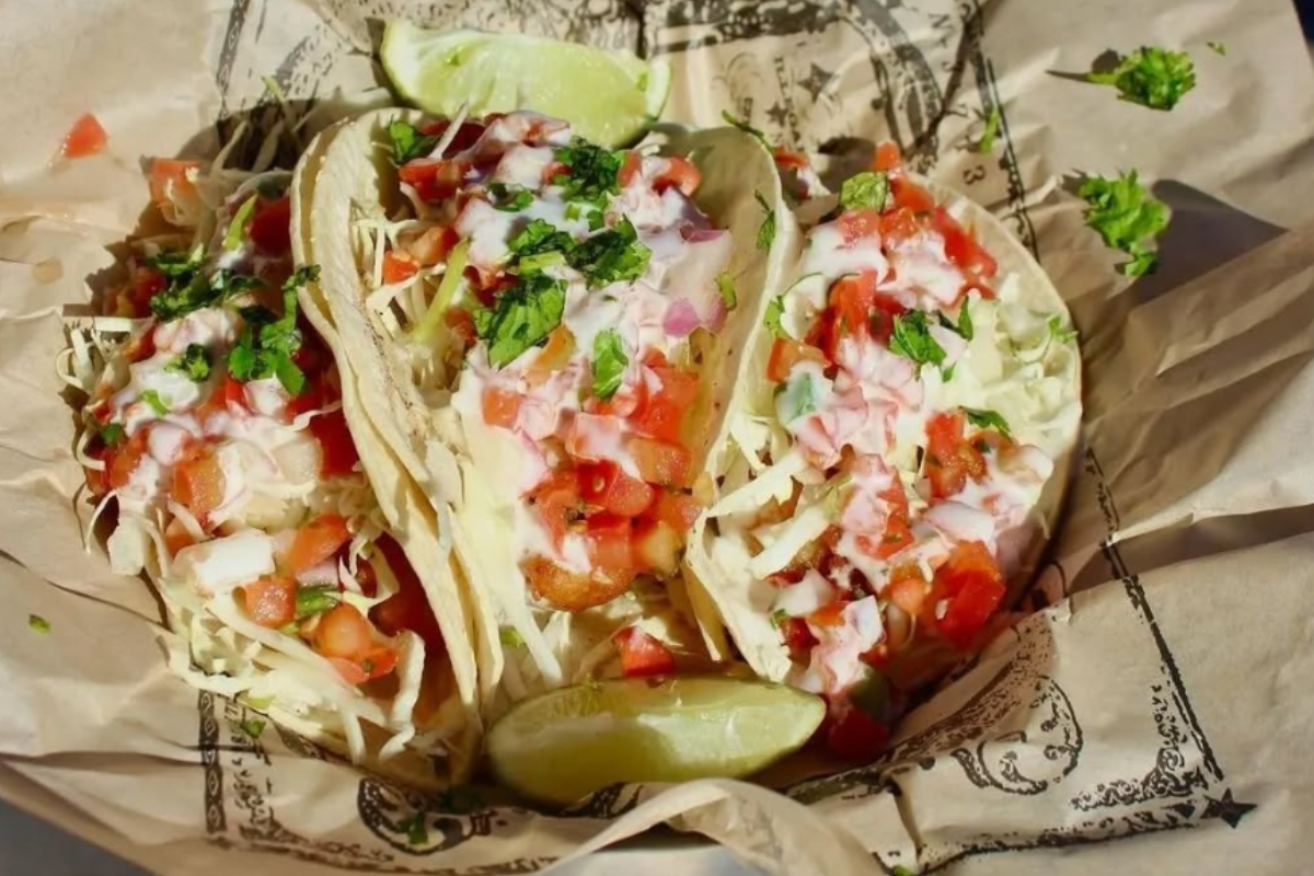 Three tacos with shredded cabbage, pico de gallo, and lime wedges at Illegal Pete’s in Denver, served in a casual foil-lined basket.