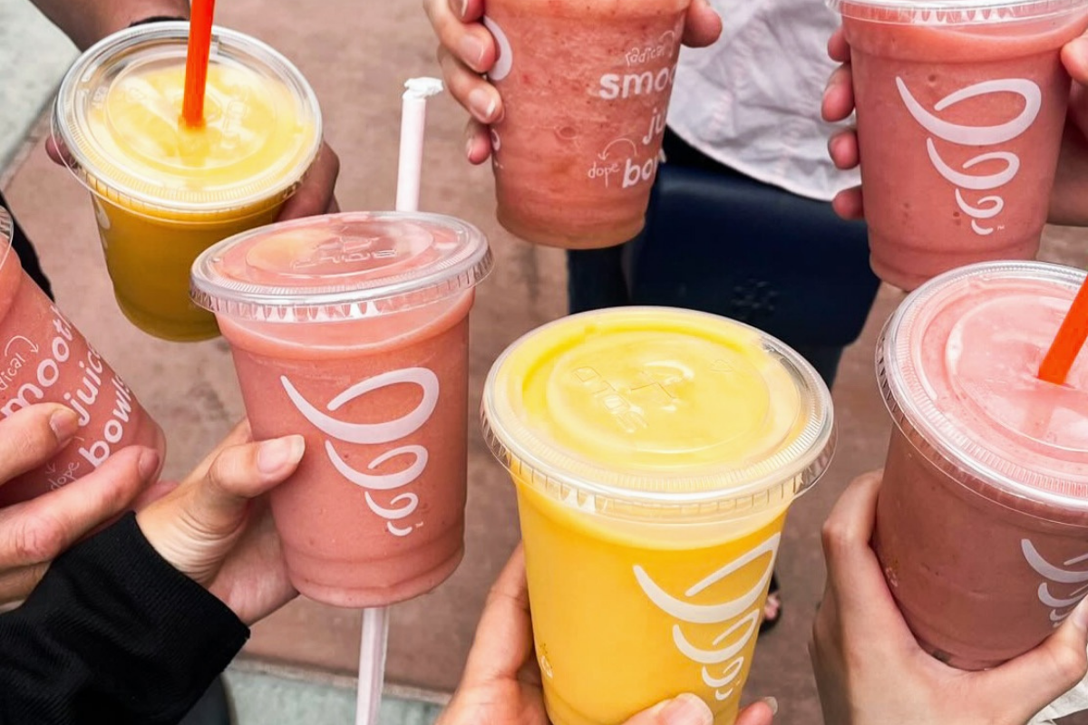 A group of people holding colorful smoothies and juices from Jamba Juice, with a mix of yellow and pink drinks in clear plastic cups with lids and straws.