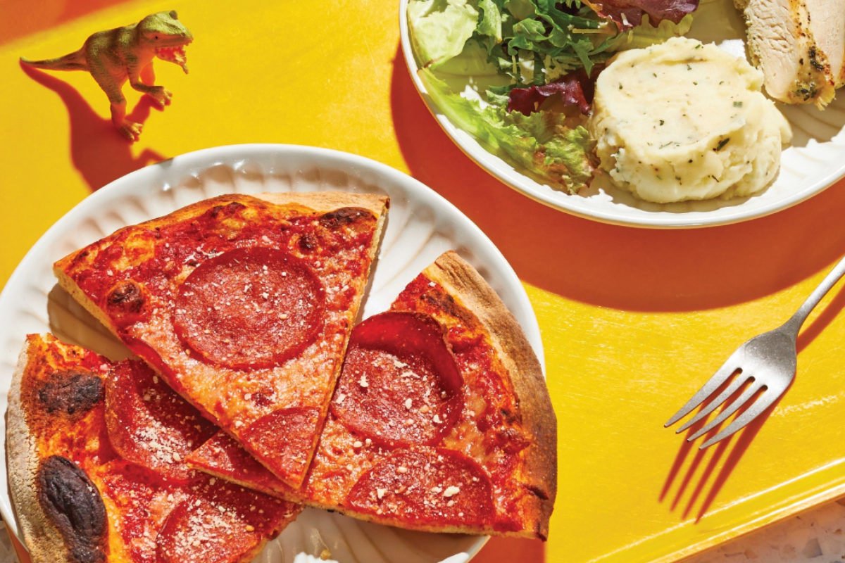 Kid’s tray with pepperoni pizza, mashed potatoes, salad, and grilled chicken from Modern Market Eatery, served on a bright yellow background.

