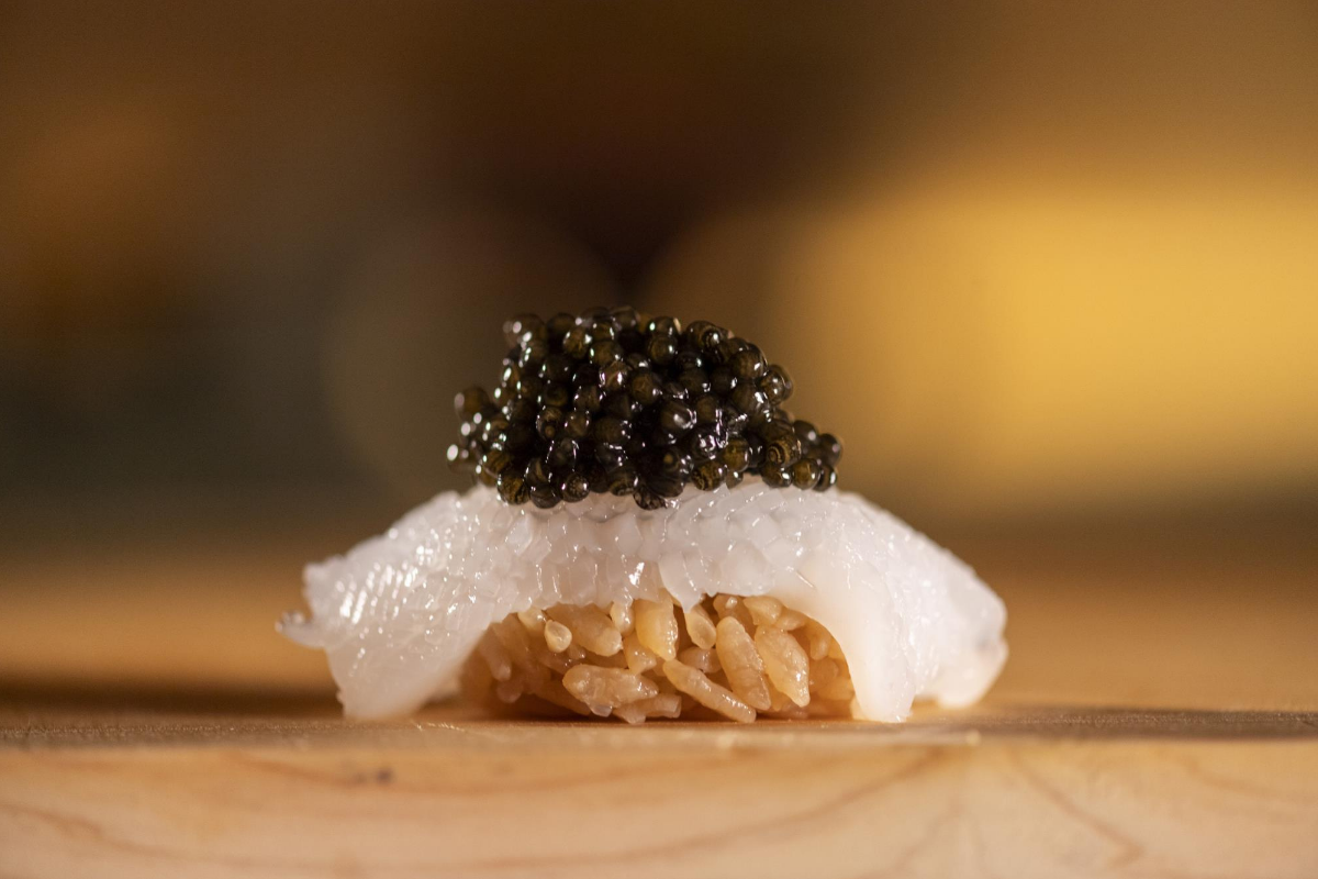 Close-up of ogawa nigiri topped with black caviar, placed on a wooden surface with a softly blurred warm background.