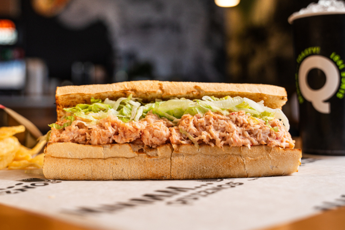 LRH Restaurant & Bar is Redefining Hotel Dining in Las Colinas - DiningOut A close-up of a Quiznos sub sandwich filled with tuna salad and shredded lettuce on toasted bread, served with potato chips and a soft drink.