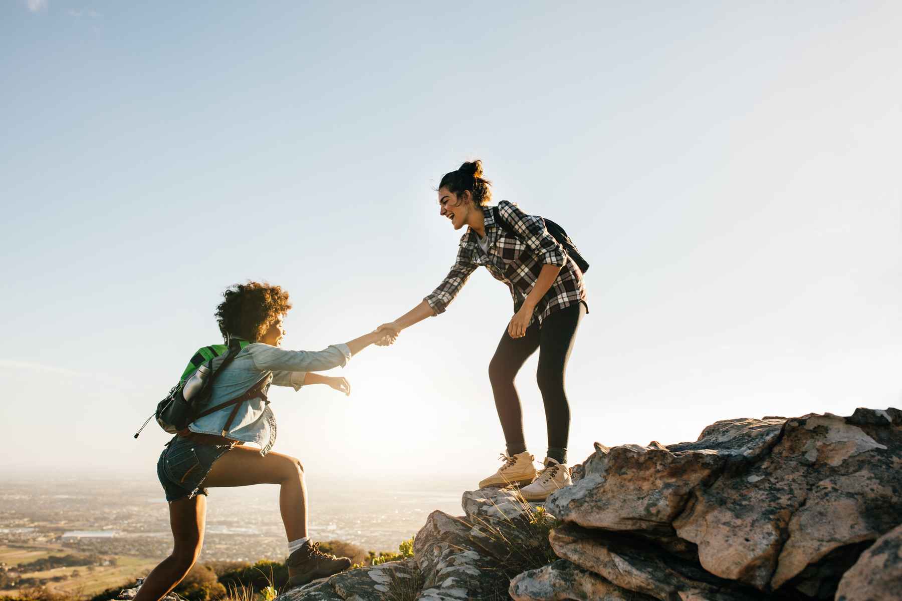 Two women climbing a mountain. One offering a helping hand to the other. Assistance during hard times