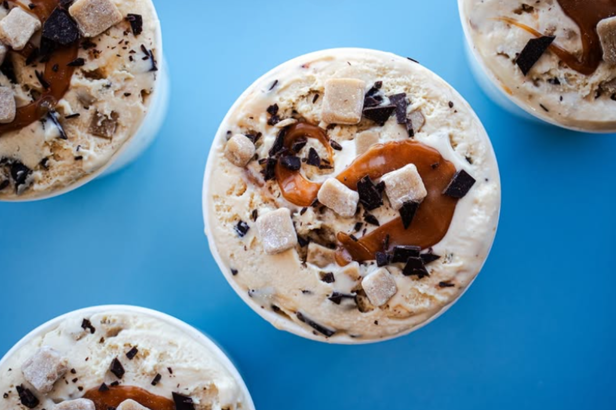 Filet - DiningOut Top view of Sadboy Creamery pints filled with caramel swirls, chocolate chunks, and cookie dough pieces, set against a bright blue background.