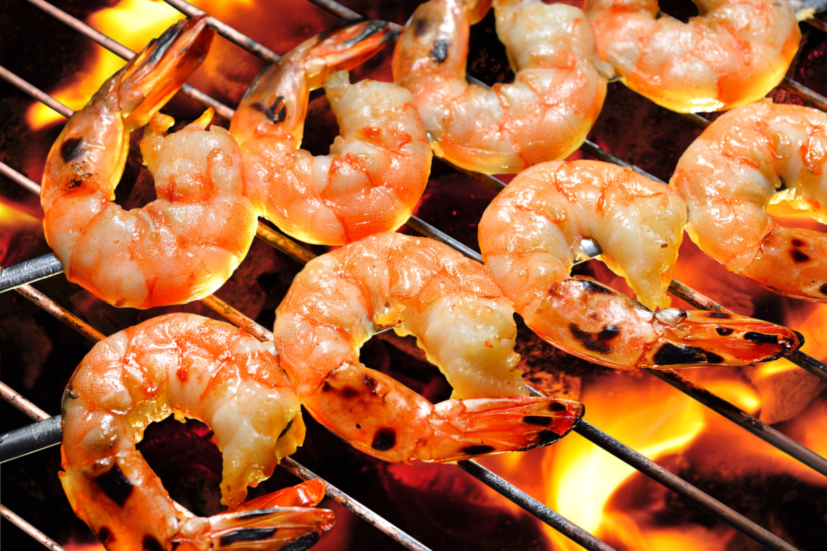 - DiningOut Grilled shrimp skewers cooking over an open flame, with char marks and a golden, juicy texture, capturing the heat and flavor of a barbecue grill.