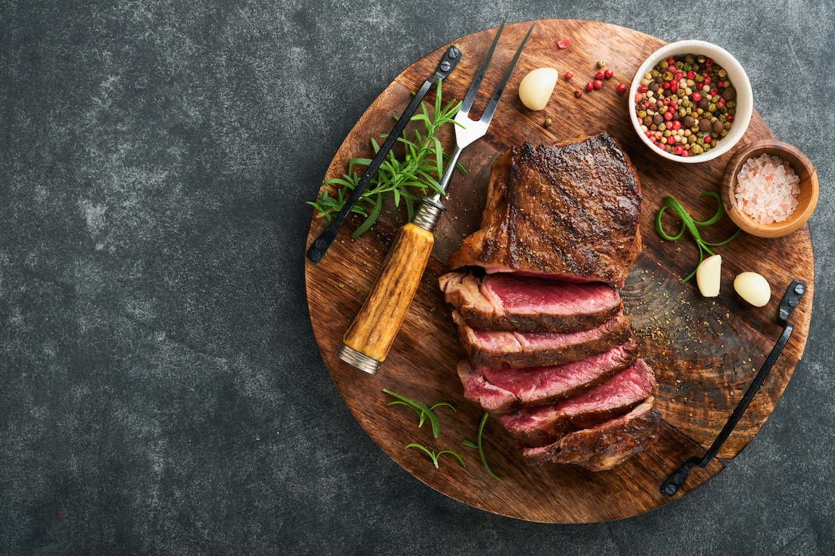 Steaks. Sliced grilled meat steak New York or Striploin with spices rosemary and pepper on black marble board on old stone grey background. Top view. Mock up.