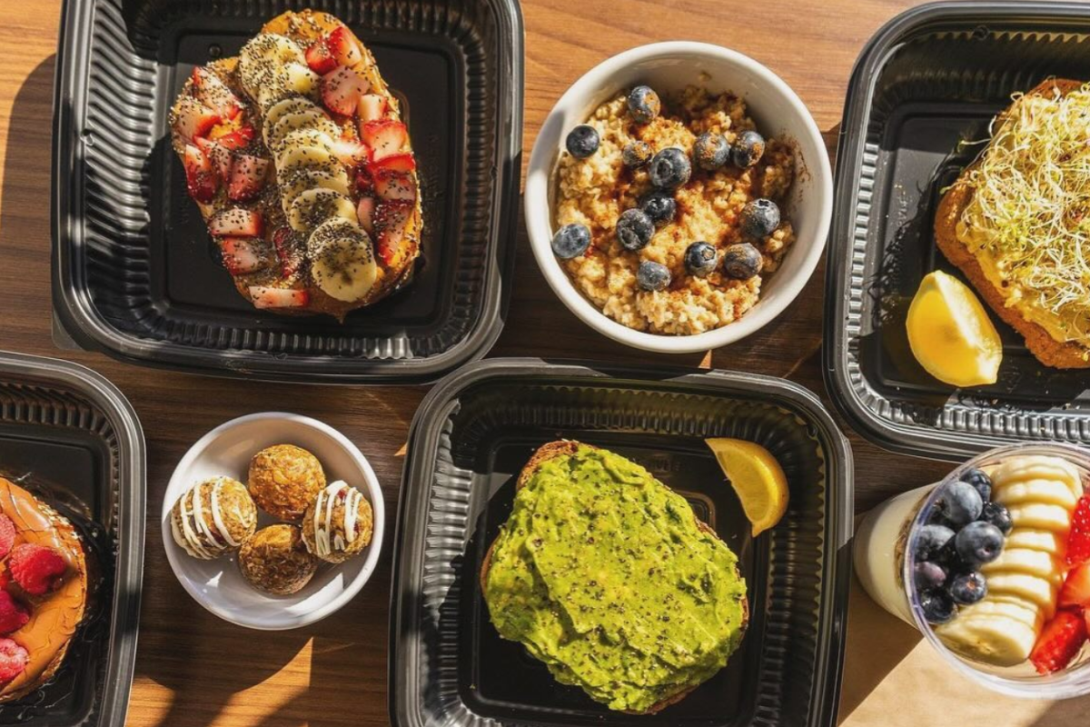 Food Trucks in Dallas You Need to Know About - DiningOut Superfruit Republic breakfast spread with avocado toast, oatmeal with blueberries, fruit-topped toast, yogurt parfait, and energy bites in black containers.