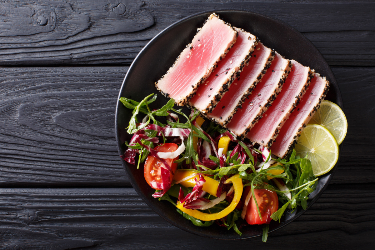 - DiningOut Close up of rare seared Ahi tuna slices with fresh vegetable salad on a plate. Top view from above horizontal