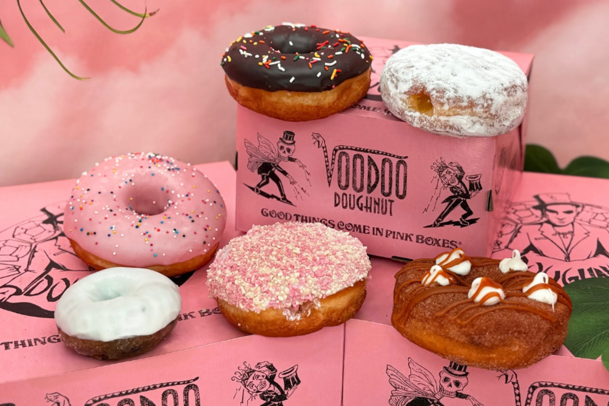Voodoo Doughnut’s colorful variety of donuts displayed on signature pink boxes, including chocolate glazed, powdered, and sprinkle-covered options.
