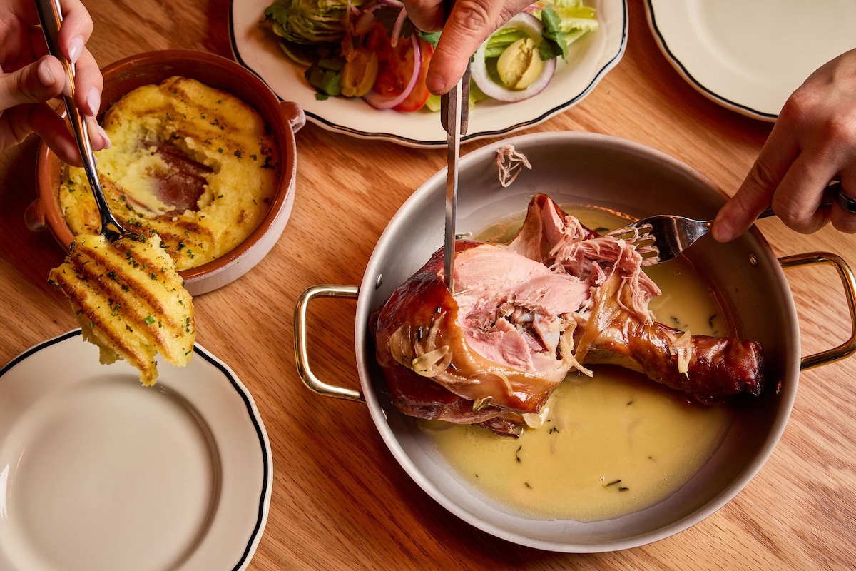 Restaurant with bright blue front door and patio with umbrellas and patio tables along sunny sidewalk.