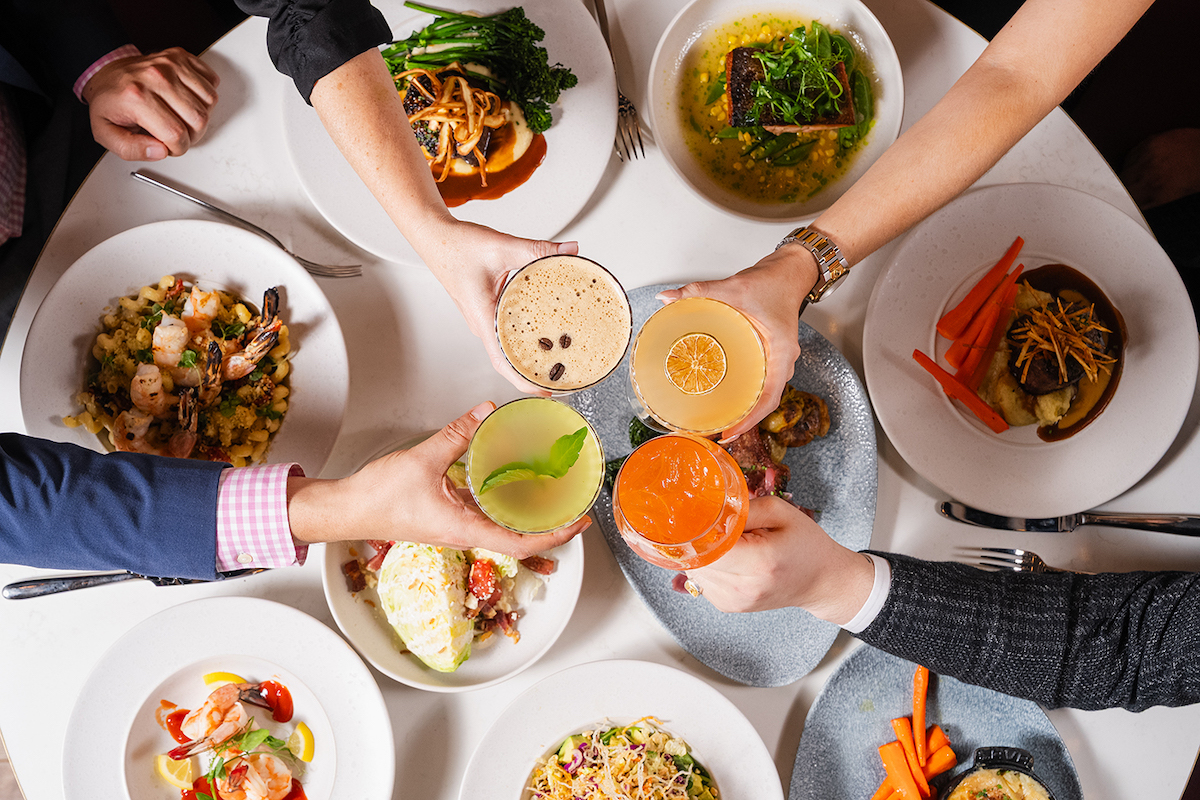 A cocktail cheers over a full spread at ASTRA Kitchen + Lounge. | Photo by ASTRA