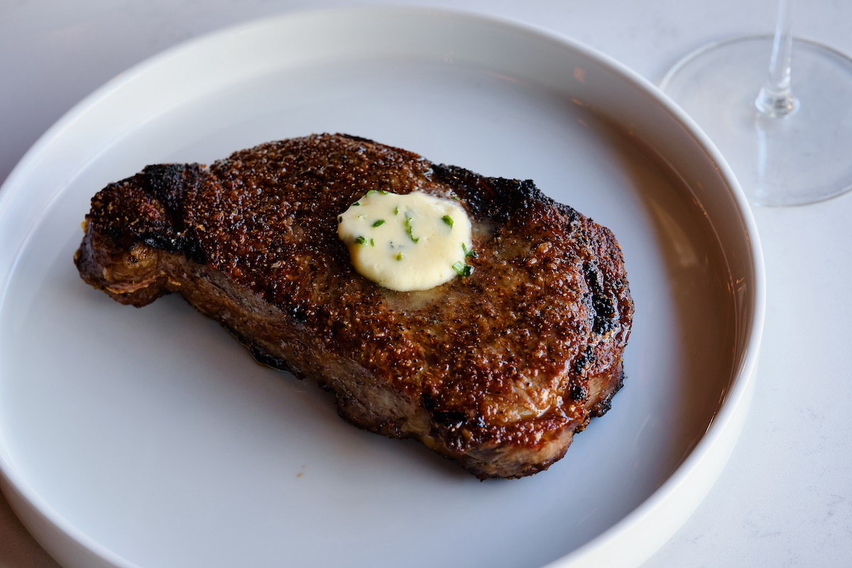 A perfectly seared steak arrives crowned with melting herb butter at Cattle Shed. | Photo by Brandon John Amato