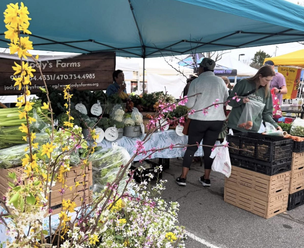 image5 - DiningOut A farmers market stall at Marietta Square Farmers Market is lined with vegetables and fresh flowers while a vendor converses with shoppers. | Photo by Marietta Square Farmers Market