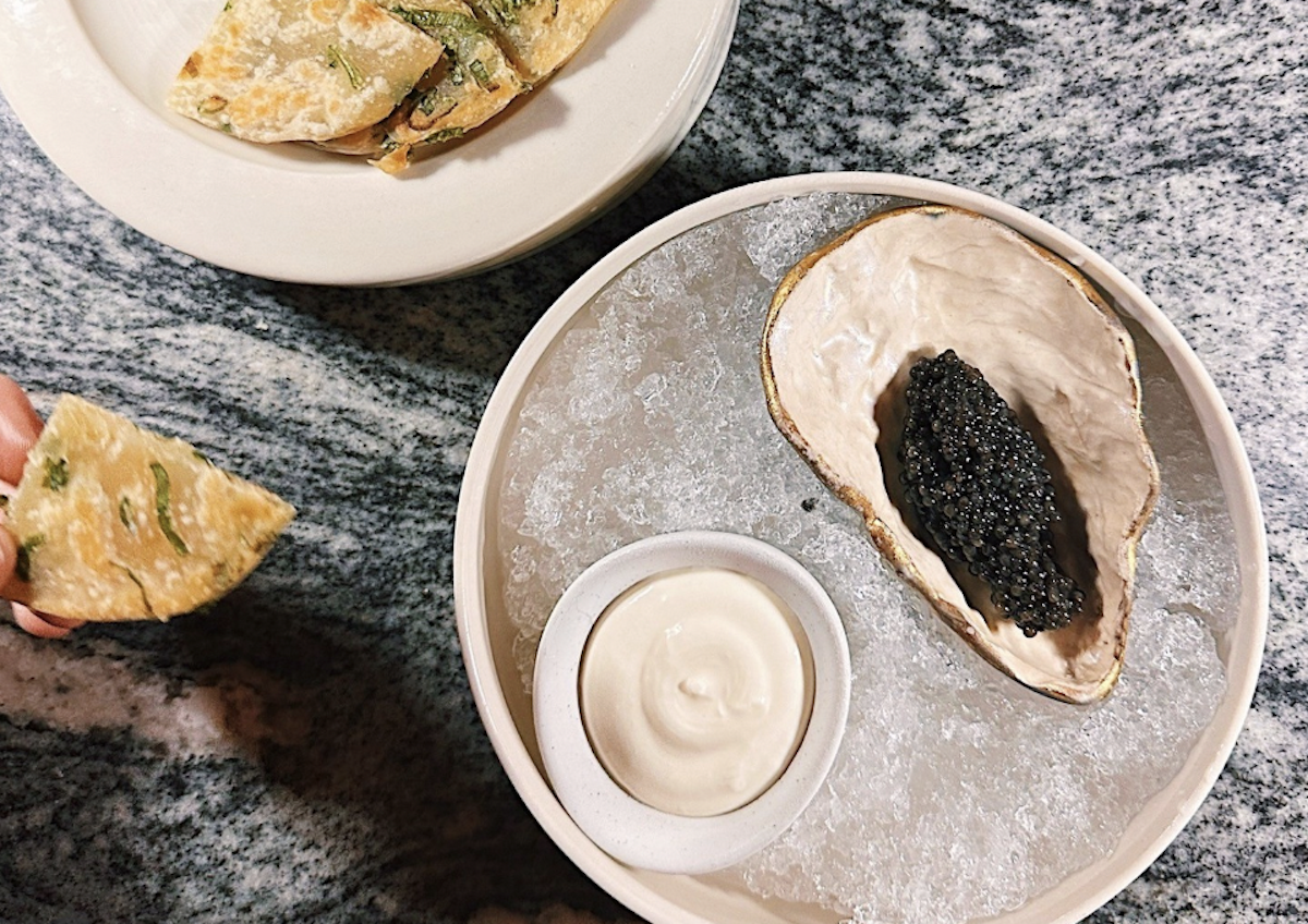 Caviar served on an oyster shell over ice, with a side of crème fraîche and scallion pancakes. | Photo by Lazy Betty