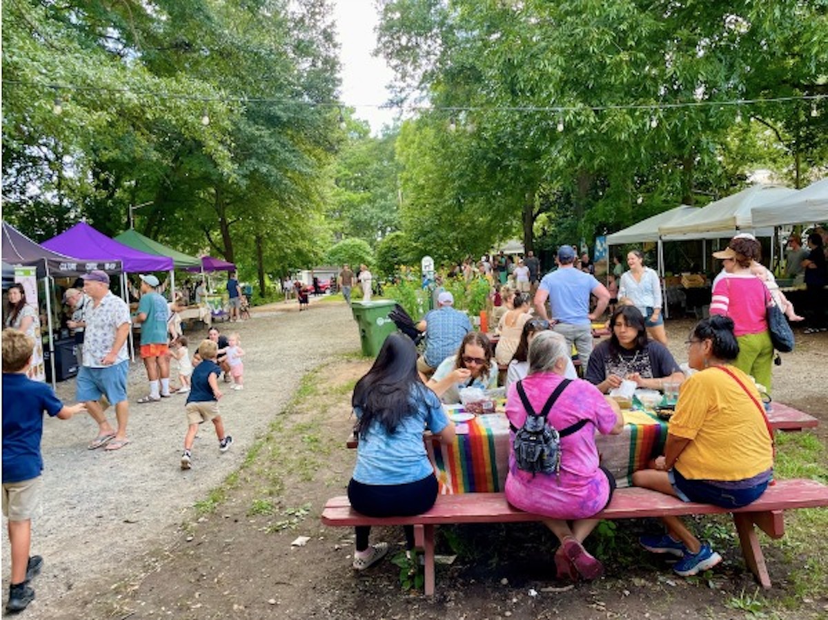image8 - DiningOut Market shoppers gather at picnic tables where vendors line a tree-covered path at East Atlanta Village Farmers Market. | Photo by East Atlanta Village Farmers Market