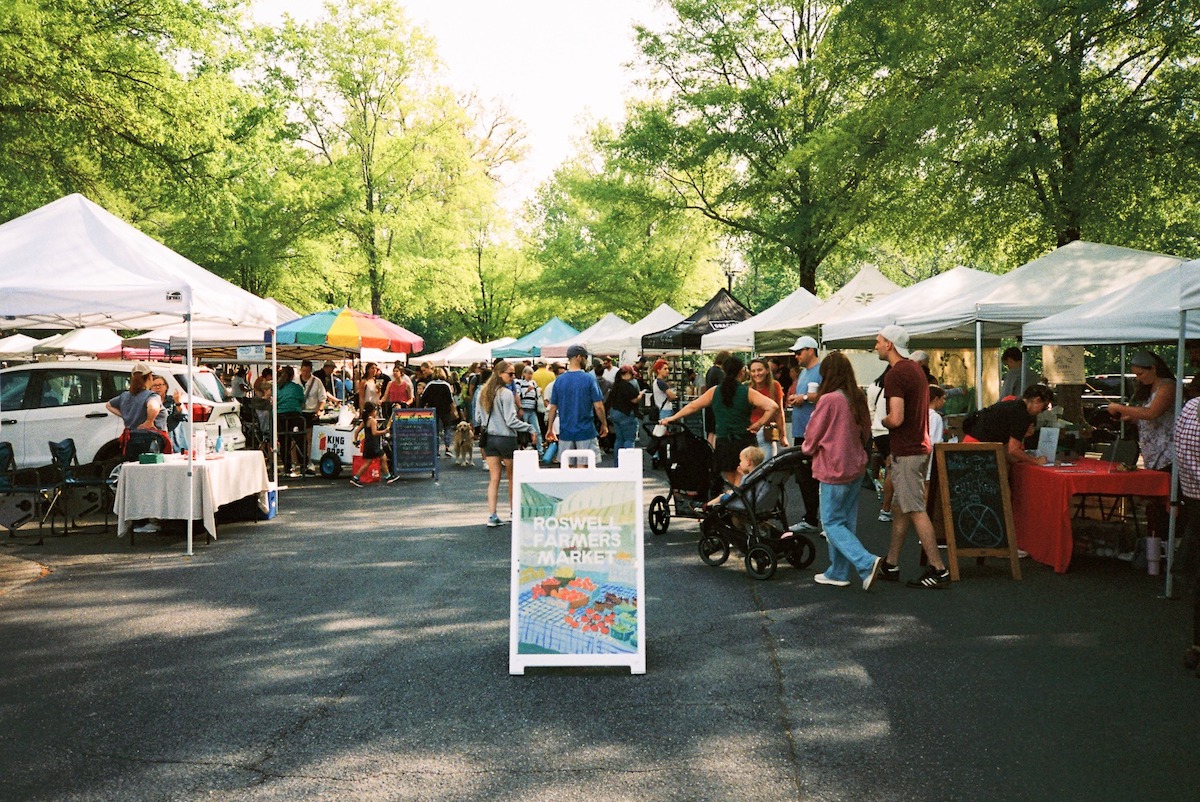 White farmers market tents line pavement with shoppers mingling and looking at products at Roswell Farmers Market. | Photo by Roswell Farmers Market