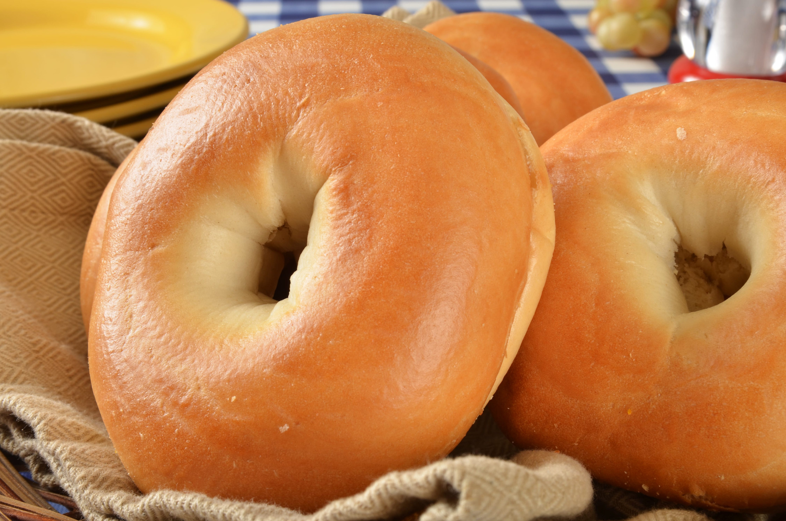 Closeup of a basket of fresh bagels with plates in the background