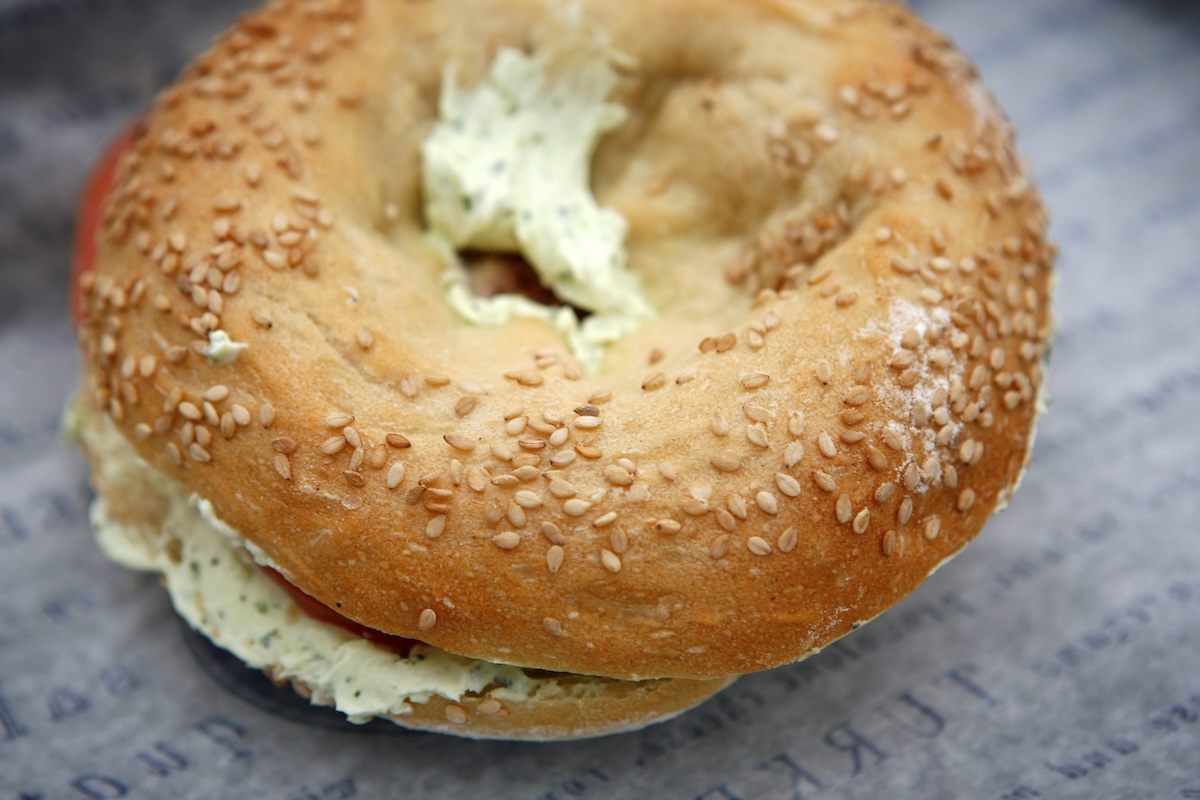 Golden-brown sesame bagel with cream cheese filling, viewed from above on a textured surface.