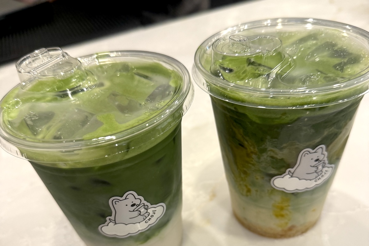 Two iced green drinks with mint leaves in clear cups, each with a white bear sticker on the side on a counter.