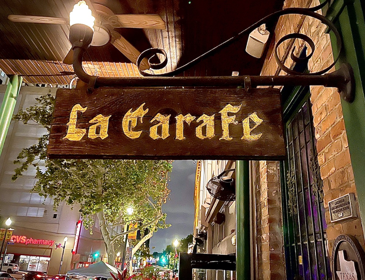 The weathered wooden sign outside La Carafe, hangs over Congress Street—marking a historic haunt known for its candlelit charm and ghostly lore. | Photo by Greg Morago