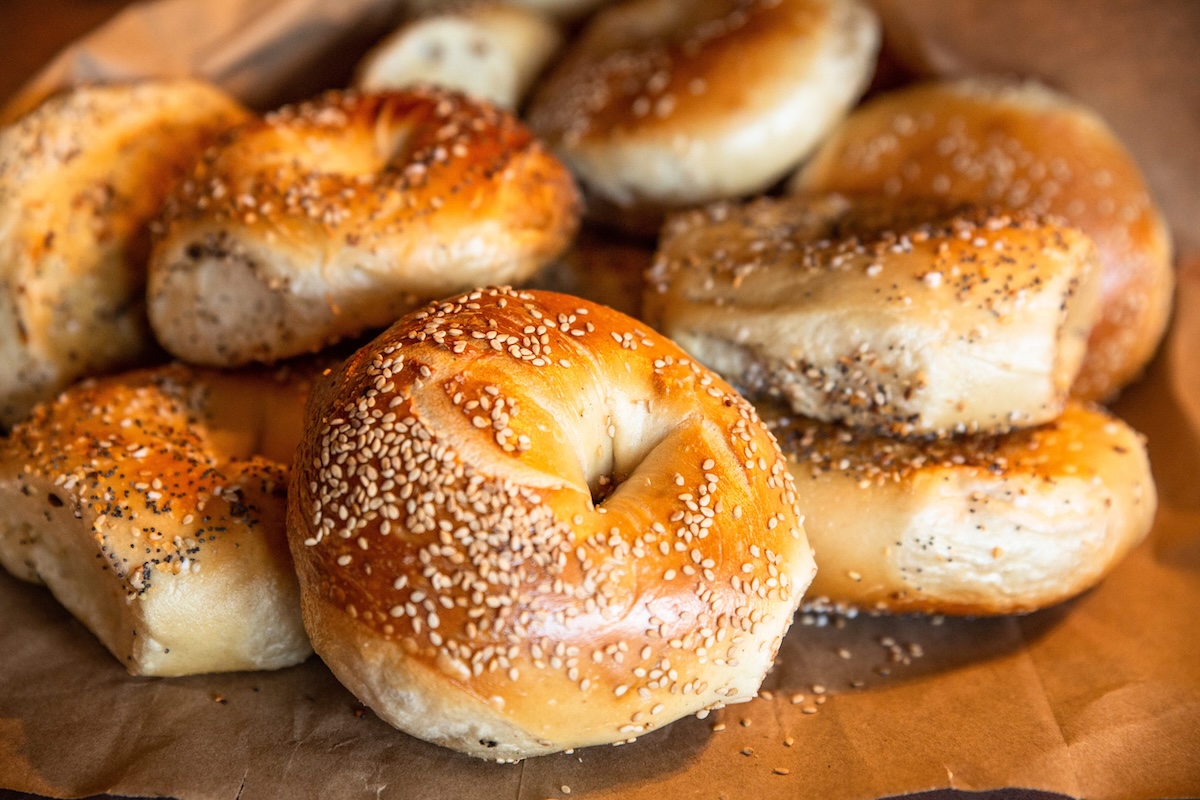 Close-up of sesame-seed bagels on brown parchment, stacked and baked to a golden brown.