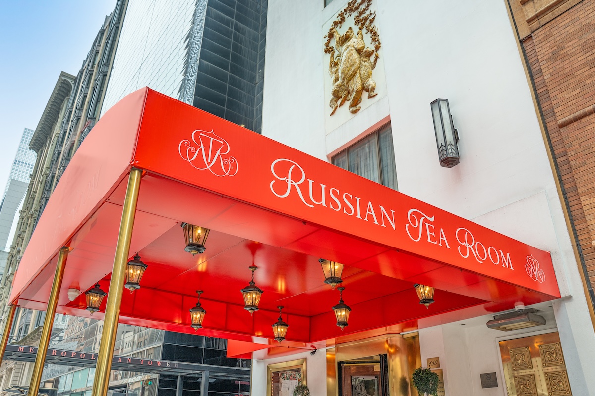 Red awning reading 'Russian Tea Room' over entrance of a building with hanging lanterns and gold-colored poles outside a city street.