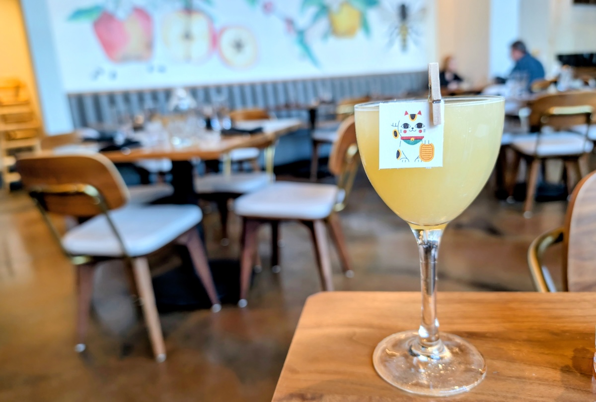 Try_Your_LUck_Apple_Blossom_by_Covington - DiningOut Try Your Luck: Kyoto Ki No Tea gin, snap pea-infused sake, housemade miso-honey syrup, fresh lemon This one was created by Apple Blossom's Restaurant Supervisor, Taylor Greenlee! The sake is infused in-house with Colorado snap peas, and the miso-honey syrup utilizes the miso featured in their Brussels sprouts sauce to create continuity between the bar and kitchen. As you saw, it features a fun Lucky CatApple Blossom's Try Your Luck cocktail with Kyoto Ki No Tea gin, snap pea-infused sake, housemade miso-honey syrup, and fresh lemon. | Photo by Linnea Covington stamp garnish.