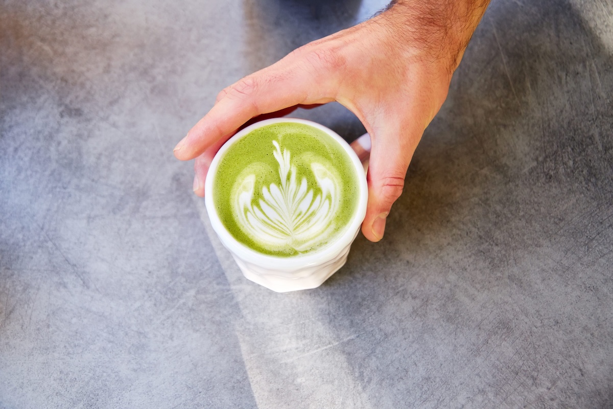 Male hand putting on table vegan matcha cappuccino with oat milk with latte art in outdoor cafe. by filirochka