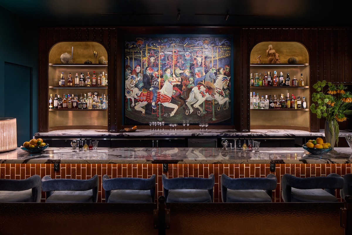 Bar Daphne’s richly layered interiors pair walnut millwork, marble, and brass accents with a striking display of curated artwork, including John Alexander’s Life on a Merry-Go-Round behind the bar. | Photo by Robert Gomez