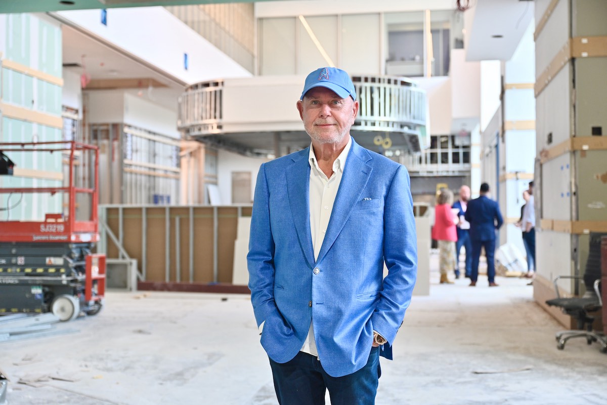 Man in a bright blue blazer and cap stands with hands in pockets inside a construction site, calm and confident.