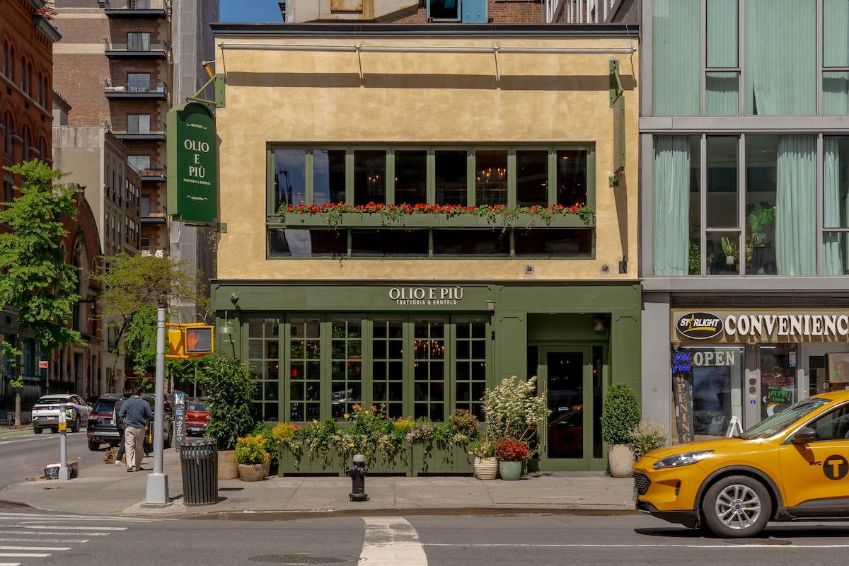 NYC_Olio e Più East Village _The_Group_Hospitality_front - DiningOut Facade of Olio e Più trattoria with green storefront and flower boxes, on a city street with a yellow taxi nearby