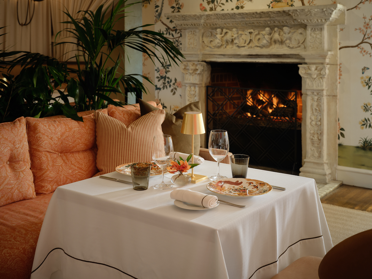An intimate fireside table at the Mansion Restaurant, where hand-carved details, warm light, and refined place settings set the stage for an elegant dining experience. | Photo by The Mansion Restaurant