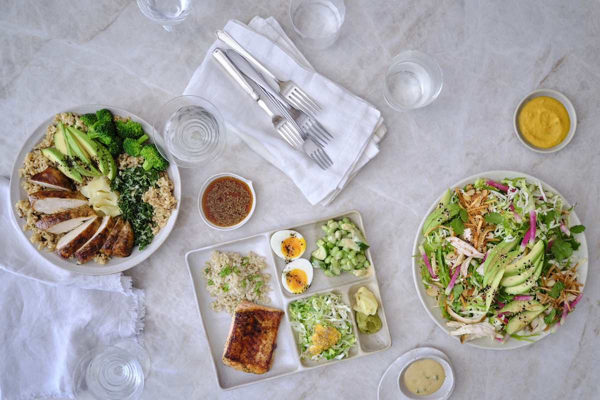 Goop Kitchen as arrived in NYC, with plans to grow. | Photo by Ditte IsagerOverhead view of a multi-dish healthy meal: sliced chicken, broccoli, avocado, and rice on a large plate, plus a separate salmon and greens plate and a fresh salad on the right.