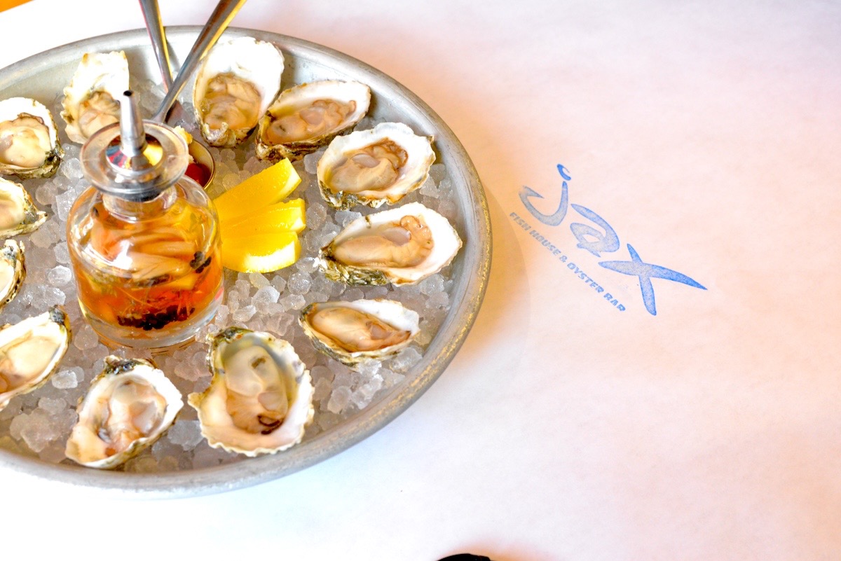 Plate of raw oysters on crushed ice with lemon wedges and a small bottle of sauce, viewed from above