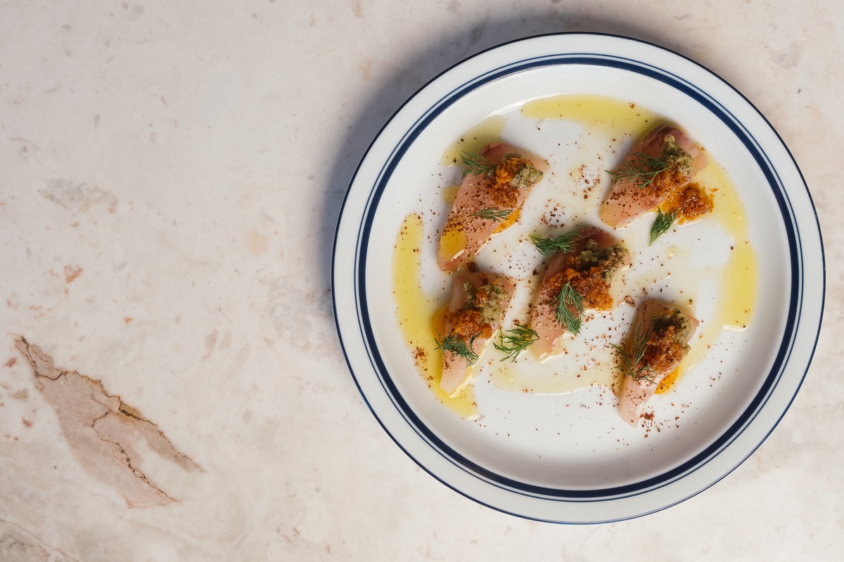 Plate of Hiramasa Crudo garnished with herbs and sauce | Photo by Chloe Vanmeveren