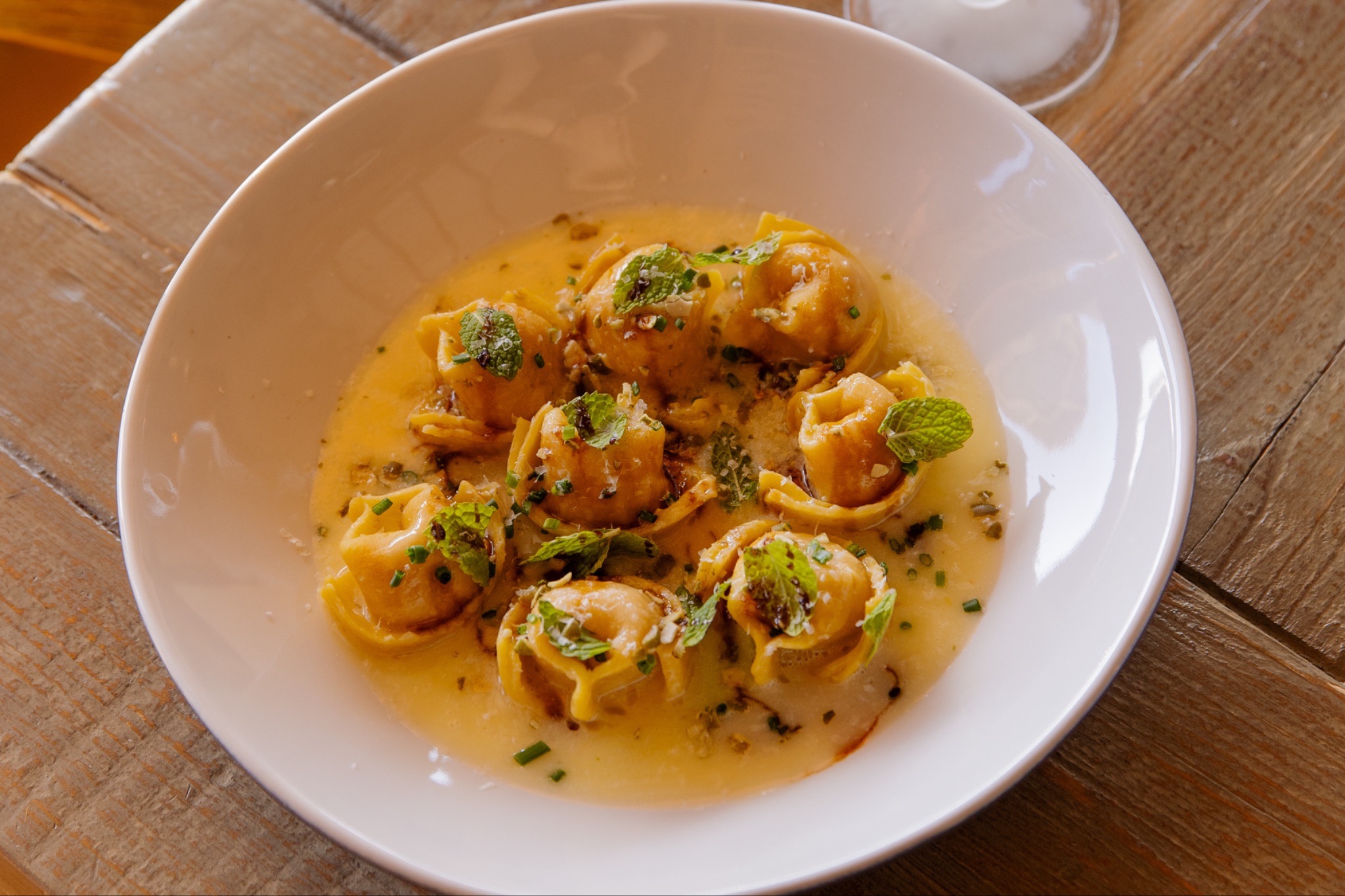 White bowl of tortellini in creamy yellow sauce, garnished with herbs. | Photo courtesy of Restaurant Progress