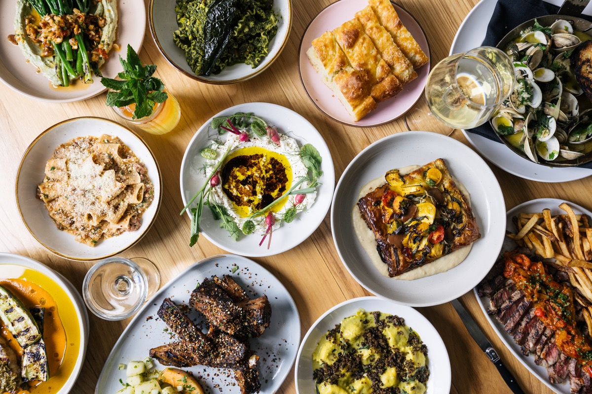 Various colorful dishes featuring appetizers, grilled meats, pasta, and white wine. | Photo by Grace Stufkosky