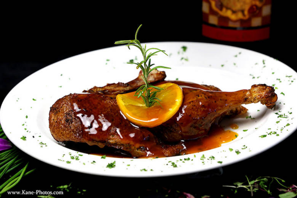 Roasted duck leg garnished with a slice of orange and rosemary | Photo by Kane Photography