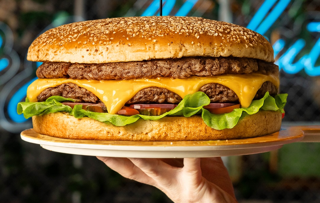 Double cheeseburger with two beef patties, melted cheddar, lettuce, and tomato on a sesame bun served on a plate