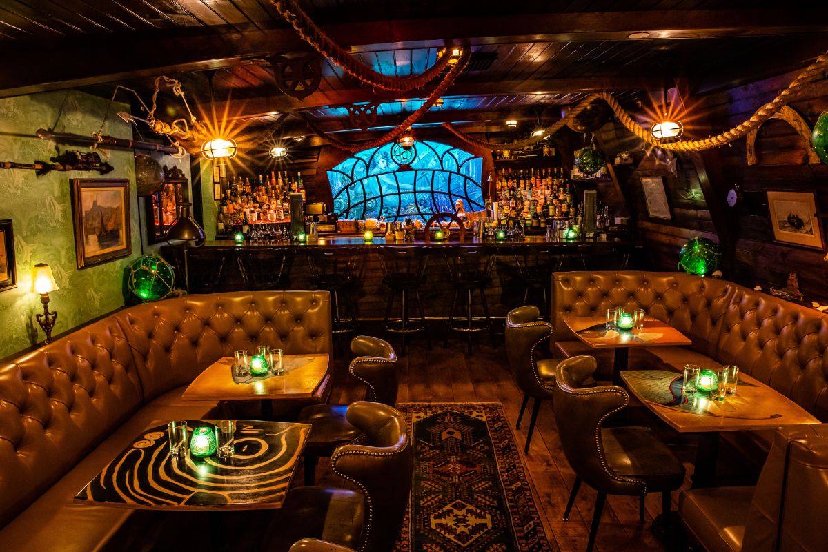 Cozy dimly lit bar with leather booths, wooden tables, and green candlelight at each table.