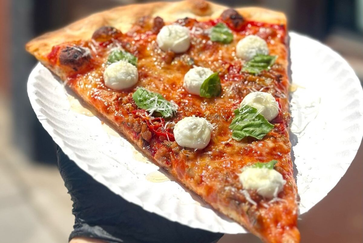 A slice of the Spicy Sausage pizza, topped with organic tomatoes, mozzarella, Schreiners sausage, Calabrian chilis, ricotta, Via's hot honey, basil, and Reggiano. | Photo courtesy of Via Della Slice Shop