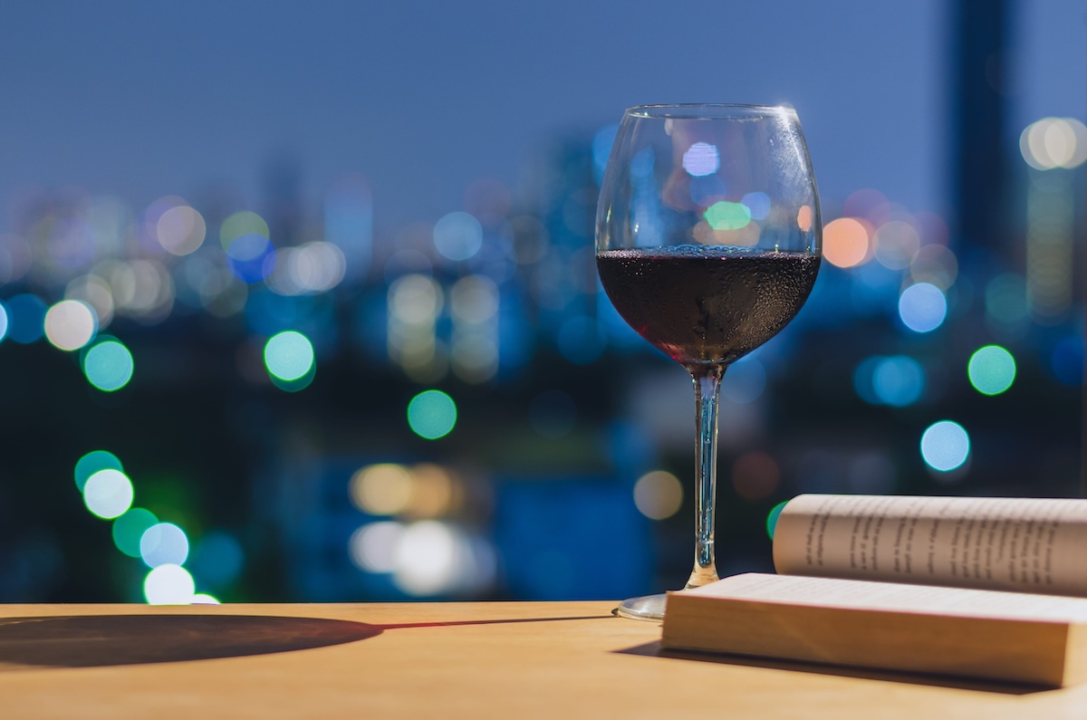 A glass of red wine on wooden table when reading book with colorful bokeh lights. Stay home concept.