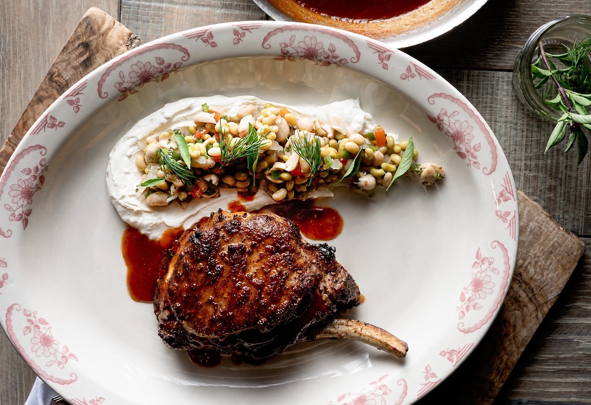Table & Main's new summer menu includes a cold-smoked bone-in pork chop served with field pea salad, grilled peach mostarda, and seasonal accompaniments from executive chef Woody Back. | Photo by Table & Main