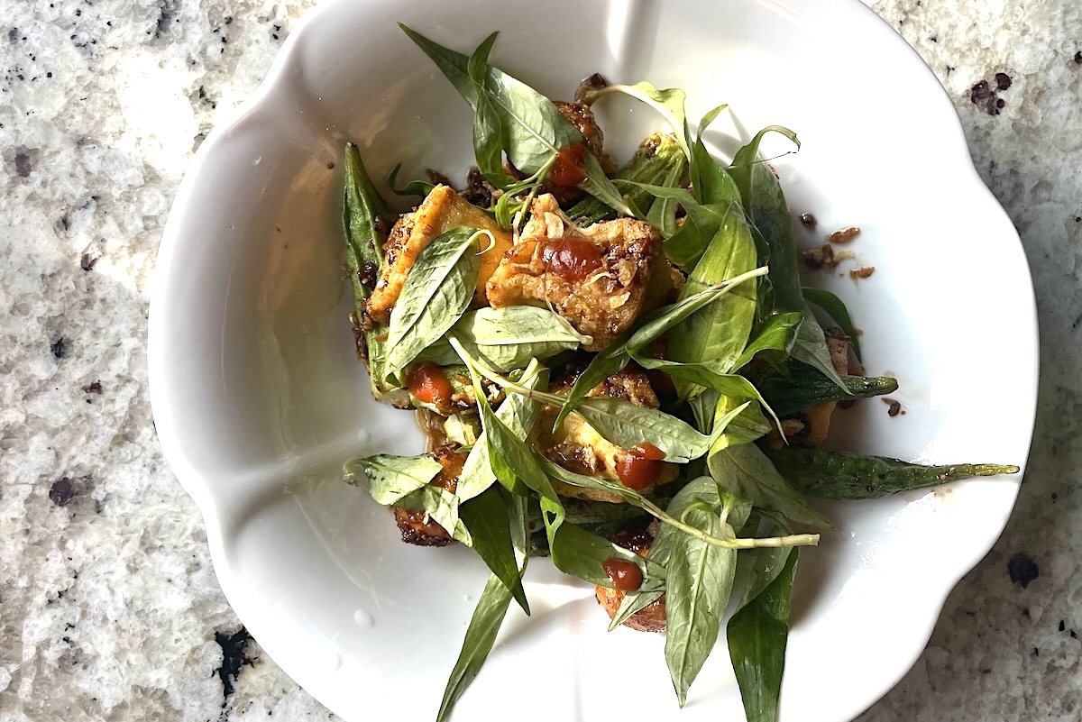 White scalloped bowl on a granite countertop, filled with a mixed greens salad including crispy fried pieces and a red sauce drizzle.