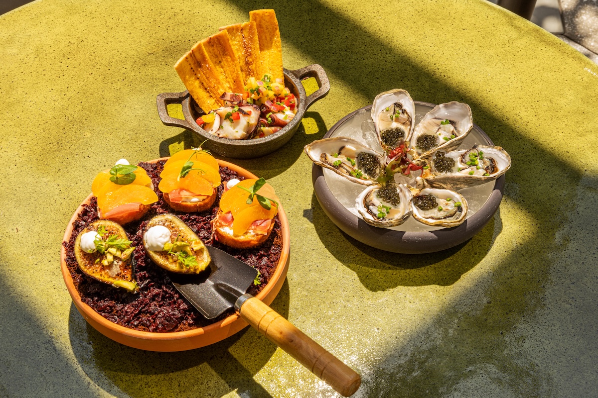 NY_DahliasGarden - DiningOut Assortment of bite-size hors d'oeuvres on a green table: peach-topped salmon crostini, avocado boats with cream, and an oyster plate with caviar.