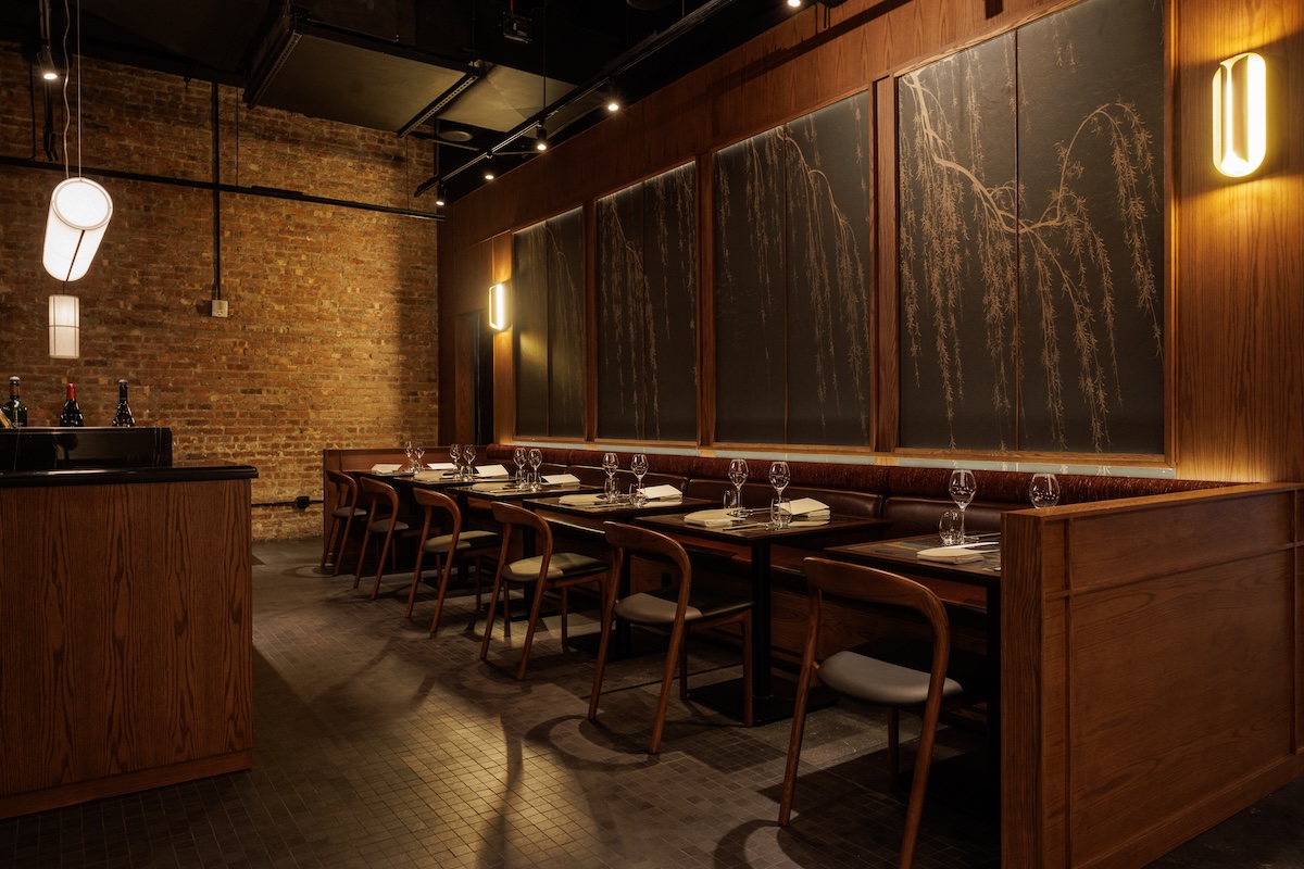 NY_Muje_ByAlexanderStein - DiningOut Cozy upscale restaurant dining area with a long wooden booth, tables set with glasses and napkins.