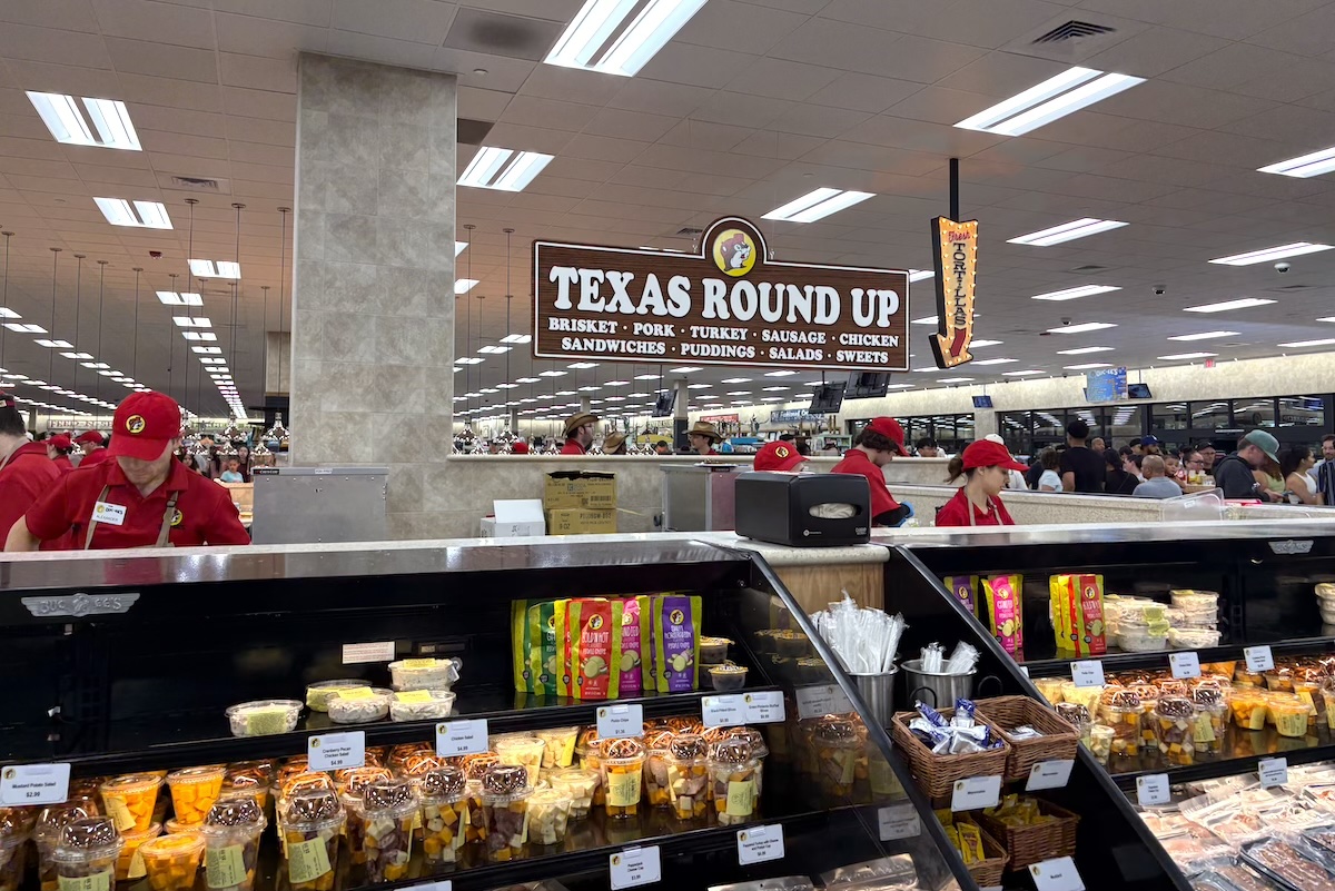 PHX_Bucees_counter - DiningOut SupermarkeBuc-ee's feels like a food hall more than a gas station store. | Photo by Photo by Michelle Talsma Eversont deli with a large 'TEXAS ROUND UP' sign above the counter and staff in red uniforms serving customers.